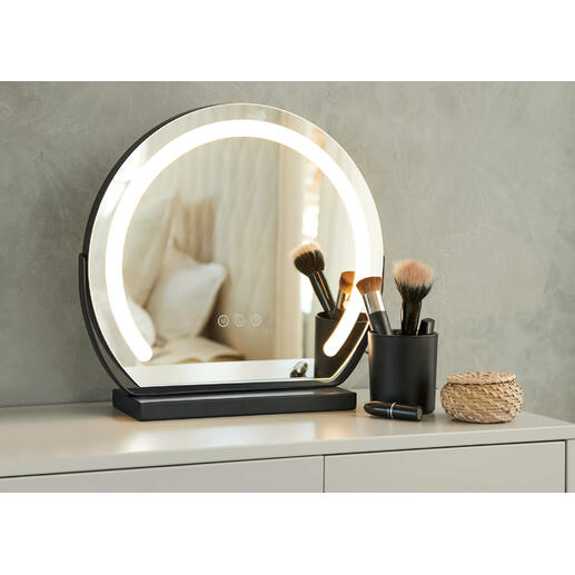Miroir de maquillage rond avec éclairage sur une table, entouré d'ustensiles de maquillage.