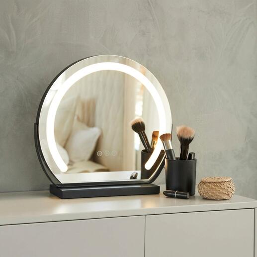 Miroir de maquillage rond avec éclairage sur une table, entouré d'ustensiles de maquillage.