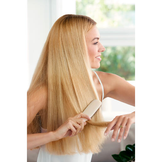 Femme aux cheveux blonds se brosse les cheveux avec une brosse à cheveux sur fond clair.