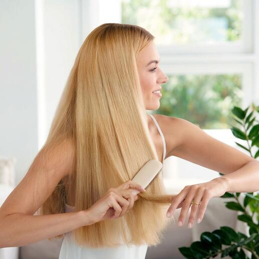 Femme aux cheveux blonds se brosse les cheveux avec une brosse à cheveux sur fond clair.