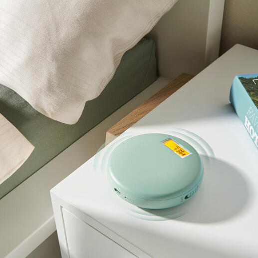 Réveil vibrant en vert doux, sur une table de nuit à côté d'un livre et d'une couette.