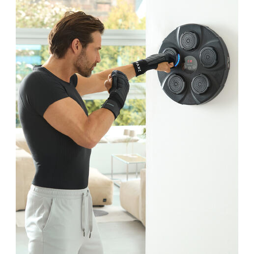 Homme frappe avec ses mains contre un boxeur mural, salle de fitness avec fenêtres lumineuses en arrière-plan.