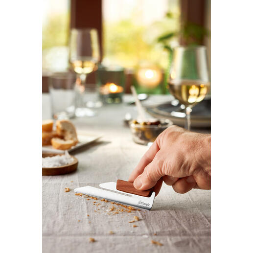 Main montrant le ramasse-miettes design sur une table dressée avec des collations.