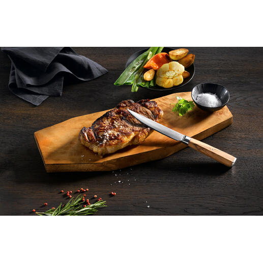 Couteau à steak en damas sur une planche en bois avec un steak grillé et des légumes.