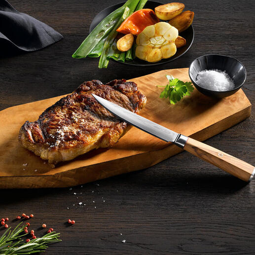 Couteau à steak en damas sur une planche en bois avec un steak grillé et des légumes.