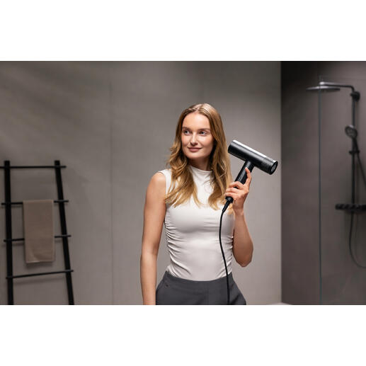 Femme tenant un sèche-cheveux noir dans une salle de bain moderne.