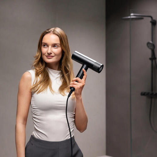 Femme tenant un sèche-cheveux noir dans une salle de bain moderne.