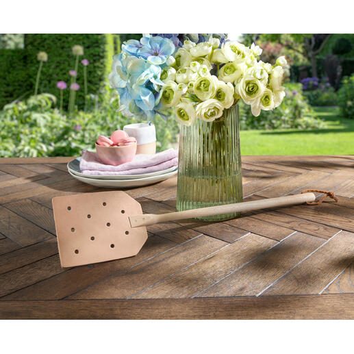 Fouette à mouches en cuir posée de manière décorative sur une table en bois rustique.