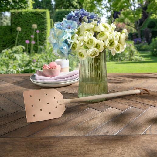Fouette à mouches en cuir posée de manière décorative sur une table en bois rustique.