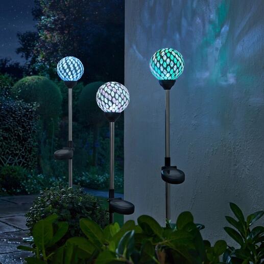 Trois piquets solaires avec des lampes en mosaïque colorées dans le jardin.