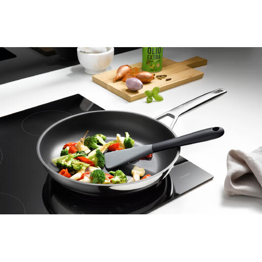 Spatule en silicone flexible dans une poêle avec des légumes mélangés.