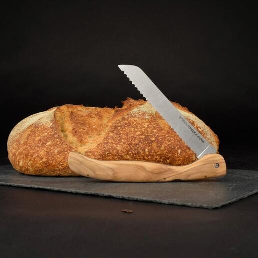 Couteau à pain pliable avec manche en bois d'olivier à côté d'un pain sur un fond noir.