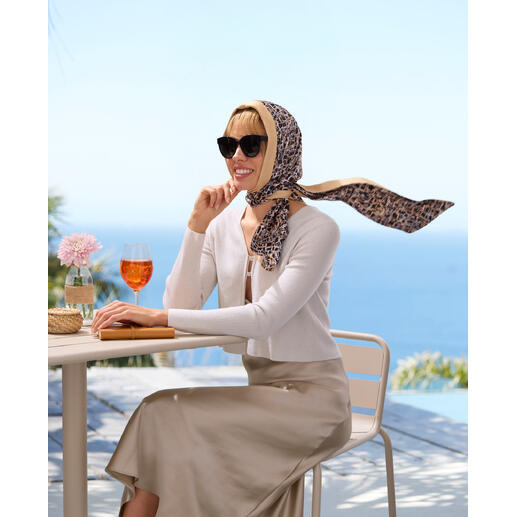 Femme assise à une table avec un apéritif, portant un foulard à motifs et des lunettes de soleil.