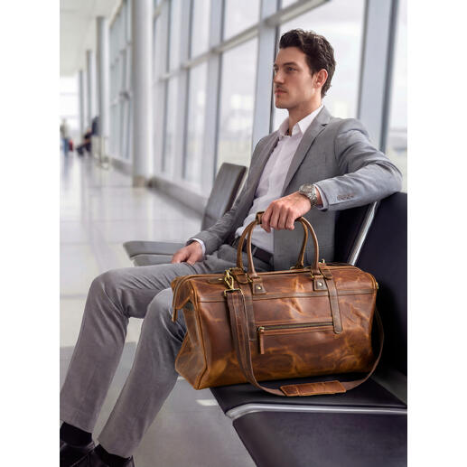 Homme assis à l'aéroport avec un weekender en cuir de buffle à côté.