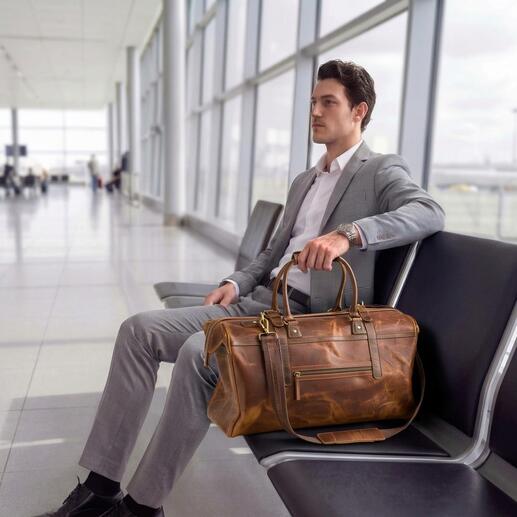 Homme assis à l'aéroport avec un weekender en cuir de buffle à côté.