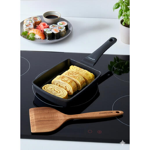 Poêle à Tamagoyaki avec des œufs enroulés à côté d'une assiette de sushi.