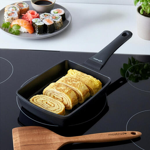 Poêle à Tamagoyaki avec des œufs enroulés à côté d'une assiette de sushi.