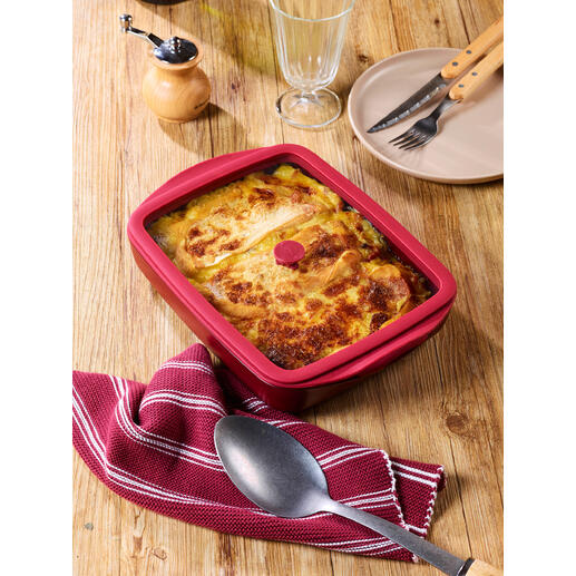 Plat à four rouge avec couvercle, rempli d'un plat de haricots, sur une table en bois.