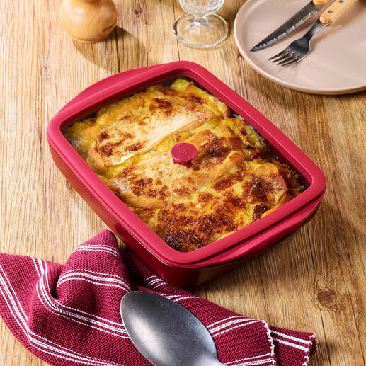 Plat à four rouge avec couvercle, rempli d'un plat de haricots, sur une table en bois.
