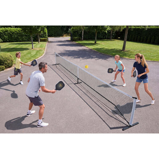 Une famille joue au pickleball en plein air, avec un filet et des balles.