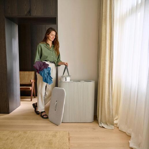 Femme avec des vêtements colorés debout à côté d'un collecteur de linge.
