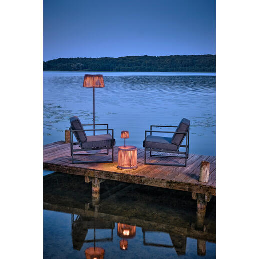Table de jardin avec éclairage LED au bord de l'eau, entourée de chaises.
