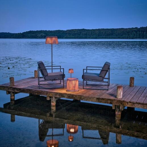 Table de jardin avec éclairage LED au bord de l'eau, entourée de chaises.