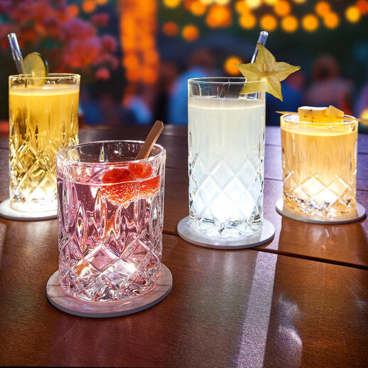 Quatre verres illuminés sur une table avec des sous-verres LED, idéaux pour une atmosphère festive.
