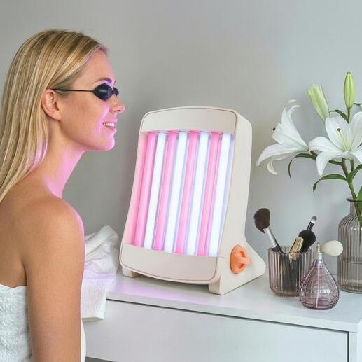 Bronzer facial avec des lampes roses et bleues, placé sur une table à côté de produits cosmétiques.