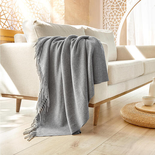 Couverture en cachemire tissée à la main drapée sur un canapé clair.