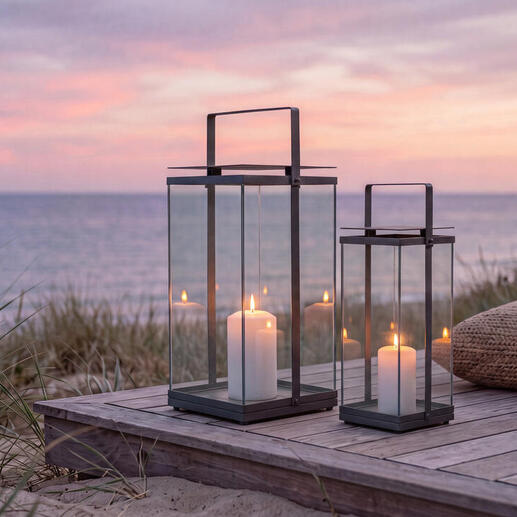 Deux lanternes design sur une terrasse en bois à la plage au coucher du soleil.