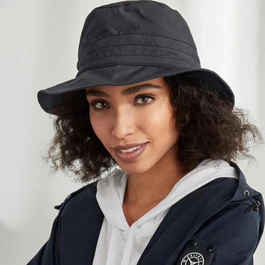 Femme portant un chapeau en coton noir pour tous les temps et un manteau gris foncé sourit à l'appareil photo.