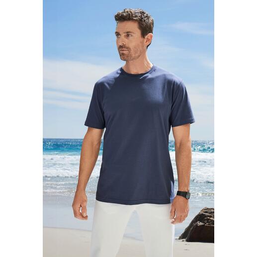 Homme en T-shirt bleu foncé se tient sur la plage face à la caméra.