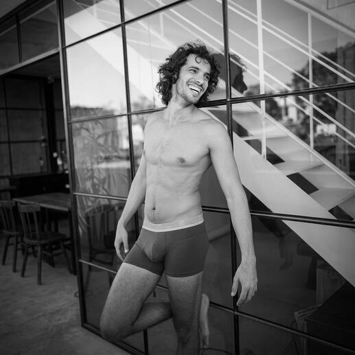 Homme en short boxer, souriant devant un mur en verre.