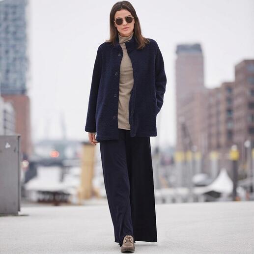 Femme dans une tenue bleu marine avec un manteau en tricot et un pantalon large dans un paysage urbain hivernal.