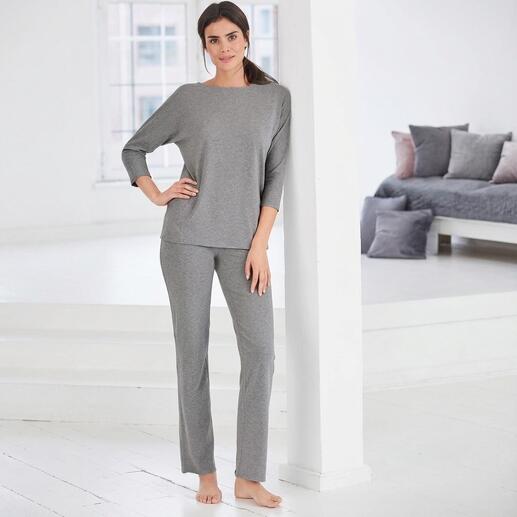 Femme en conjunto de maison gris se tient contre un mur.