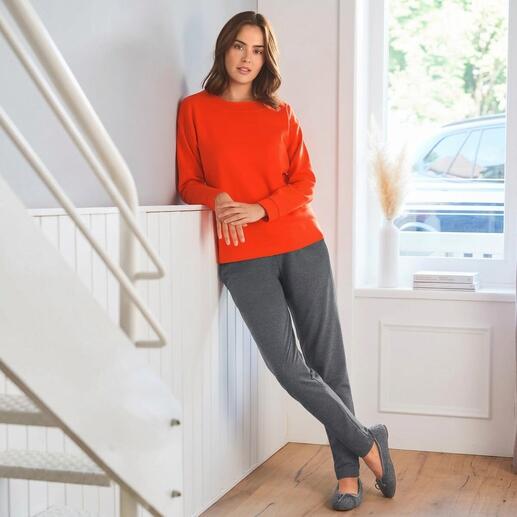 Femme en sweat-shirt rouge et pantalon de jogging gris adossée à un escalier.