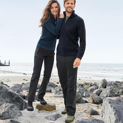 Couple en pulls marins sur la plage, entourés de pierres et de la mer.