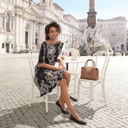 Femme dans une robe à motifs assise à une table en extérieur.