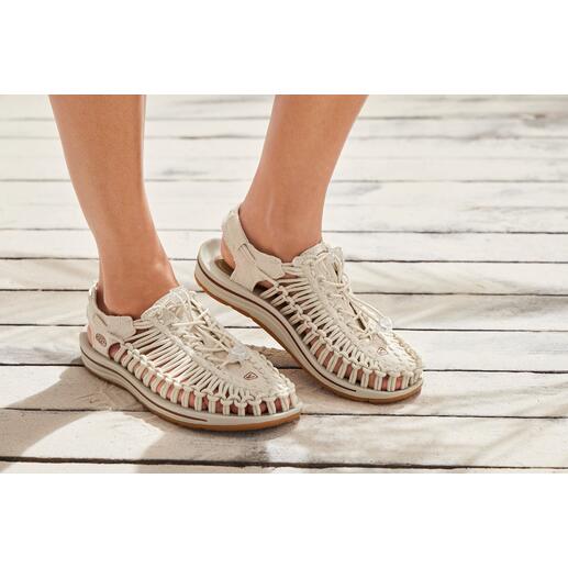 Femme et Homme, Naturel Pieds dans les sandales Outdoor Uneek de KEEN sur un sol en bois.