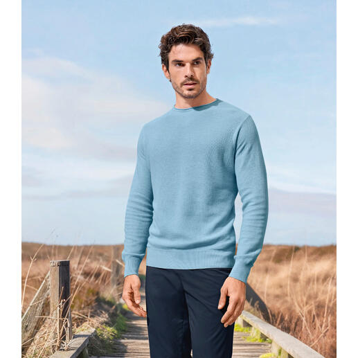 Pull noble en piqué Junghans 1954 Homme dans un pull piqué bleu clair se tenant dans un environnement rural.