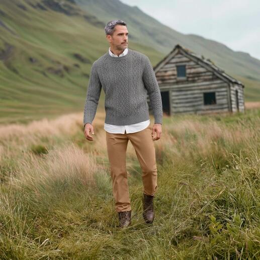 Homme portant un pull Aran gris dans un paysage verdoyant.
