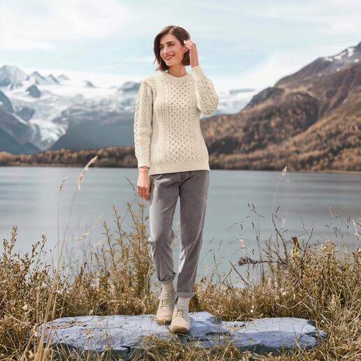 Femme en pull Merino-Aran blanc en laine au bord de l'eau avec vue sur les montagnes