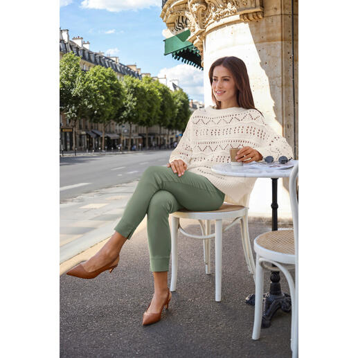 Blanc Femme en pull tricoté avec un motif à trous, assise à une table dehors avec un café.