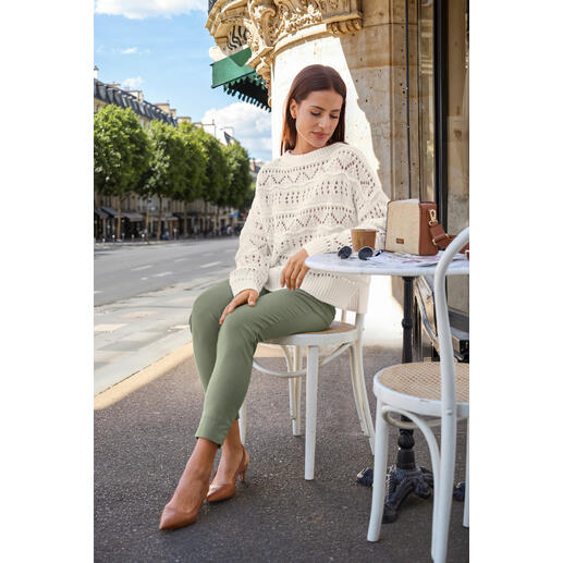 Boxy Bag en raphia Pourchet Paris Femme en pull tricoté assise à une table avec un café et un sac, avec une ville en arrière-plan.