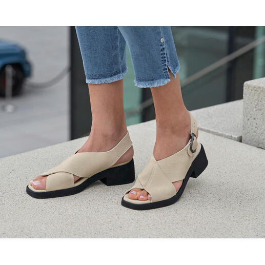Sandalettes confortables de luxe arche Sandales beige arche à talon bloc et jeans sur un sol en pierre.