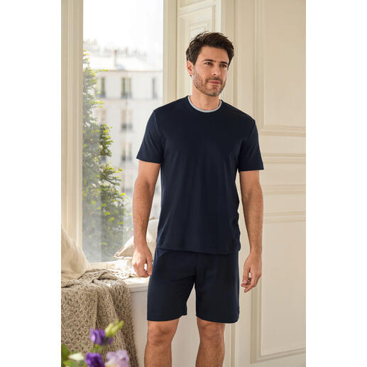 Pyjama Recovery Homme debout dans une pièce lumineuse portant un pyjama de récupération bleu marine avec un short.