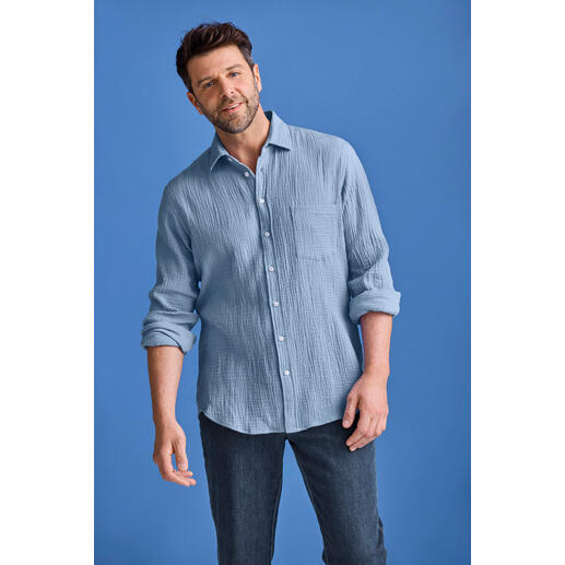 Bleu clair Homme portant une chemise en mousseline bleu clair, debout devant un fond bleu.