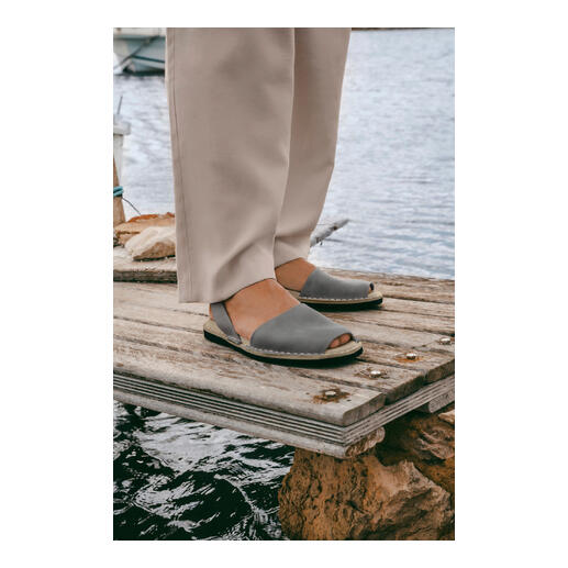Avarcas de Menorca Personne avec des Avarcas de Menorca grises sur un quai en bois au-dessus de l'eau.