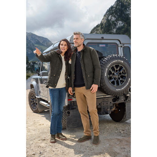Couple en vestes d'extérieur se tient devant un véhicule tout-terrain dans un environnement naturel.
